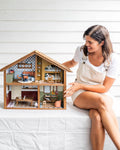 Woman sitting on a white surface with a detailed dollhouse in front of her