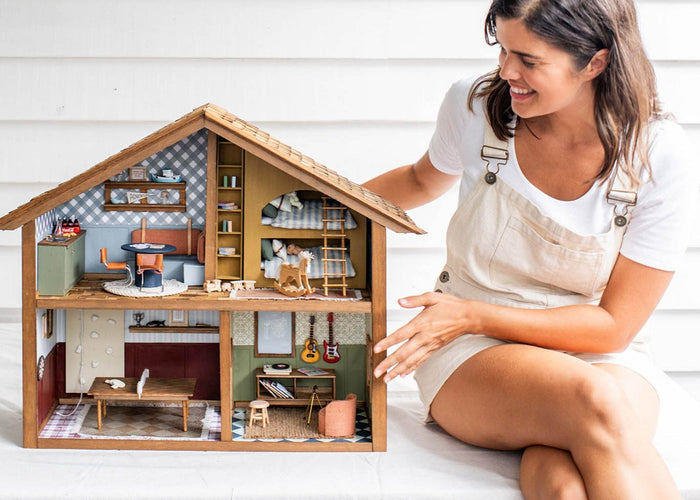 Woman sitting on a white surface with a detailed dollhouse in front of her