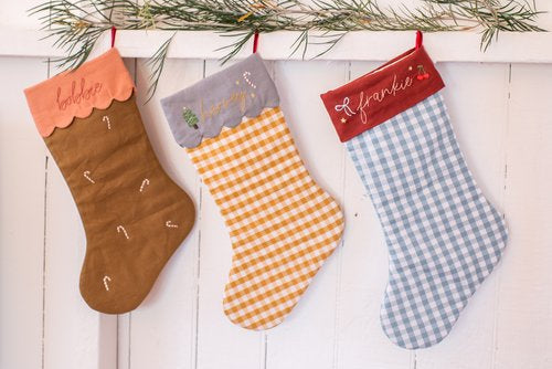 Three colorful Christmas stockings hanging on a white wooden wall with greenery.