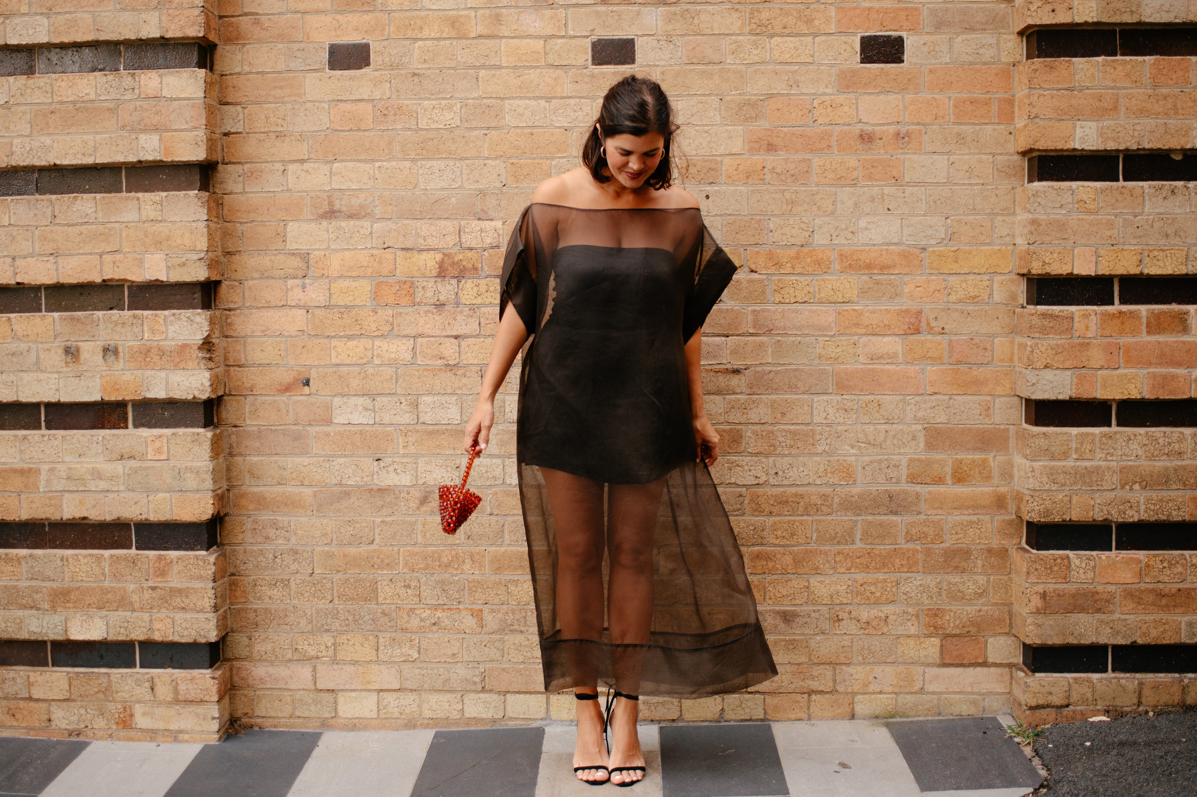 Woman wearing a black dress standing against a brick wall.